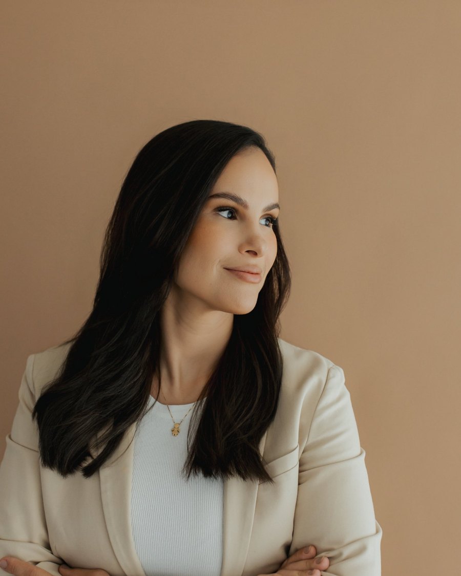 Mariana Muniz de blazer claro, braços cruzados, olhando para o lado